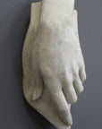 photo with gray background of plaster cast sculpture of female left hand on a curved panel with fingers curled except index finger that points