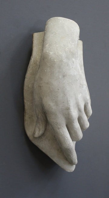 photo with gray background of plaster cast sculpture of female left hand on a curved panel with fingers curled except index finger that points