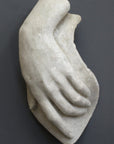 photo with gray background of plaster cast sculpture of female left hand on a curved panel with fingers curled except index finger that points