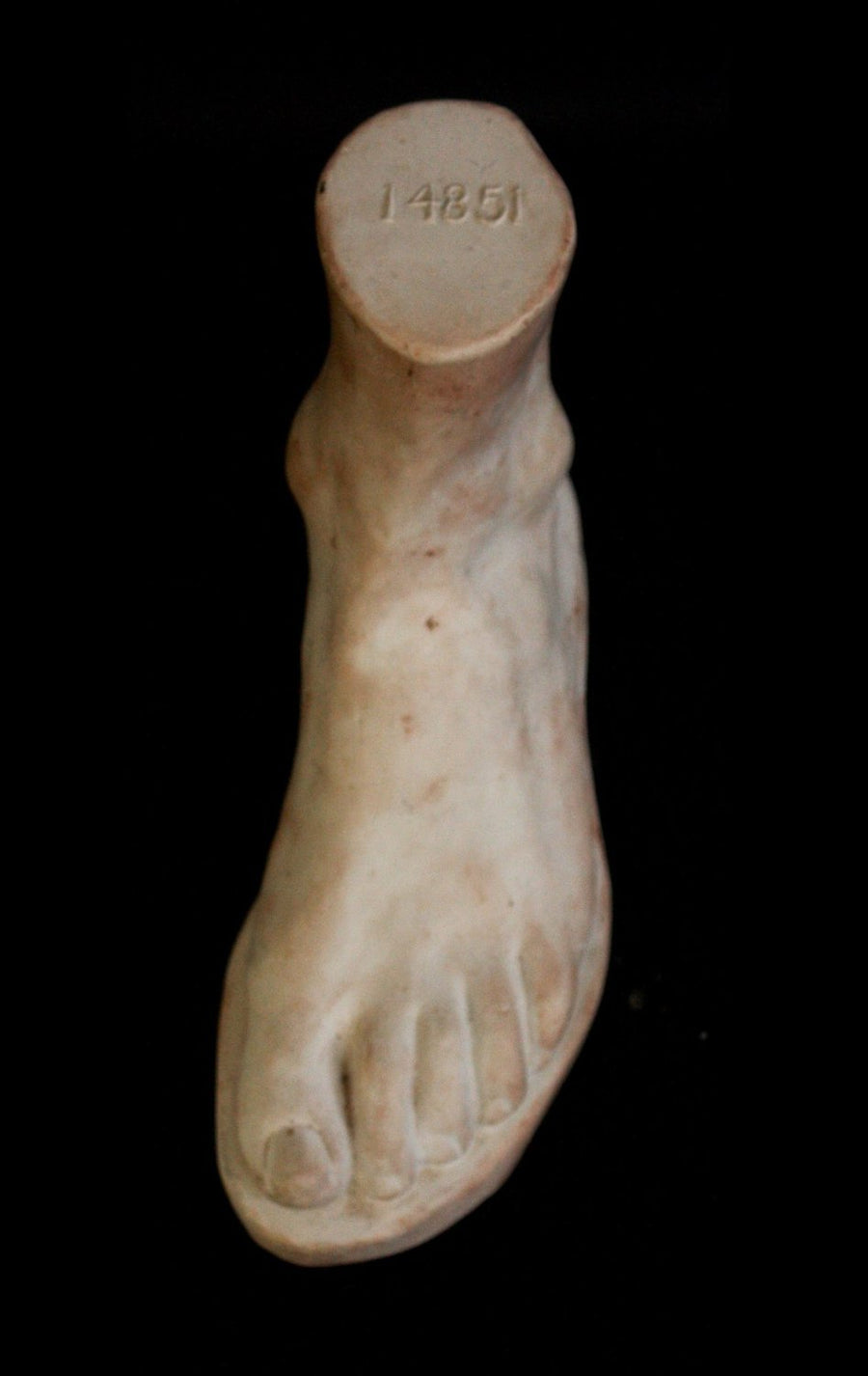 Photo of plaster cast male foot sculpture from the top on a black background