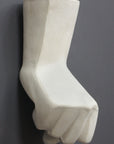 photo of white plaster cast sculpture of hand in fist in block forms against gray background