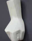 photo of white plaster cast sculpture of hand in fist in block forms against gray background