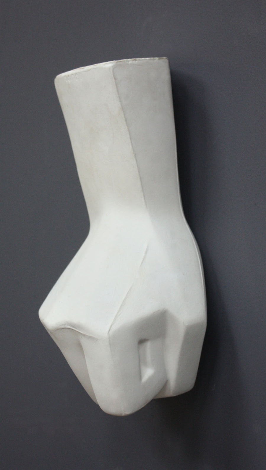 photo of white plaster cast sculpture of hand in fist in block forms against gray background
