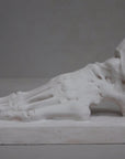 photo of white plaster cast sculpture of flayed left foot on a rectangular base against gray background