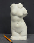 photo of off-white plaster cast sculpture of female torso and yellow pencil beside it against dark gray background