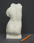 photo of off-white plaster cast sculpture of female torso and yellow pencil beside it against dark gray background