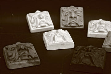 Photo with black backdrop of 7 square tile sculptures of faces made of leaves with different expressions