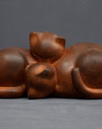 Photo with gray background of brown plaster cast sculpture of two cats sleeping with their heads nestled together
