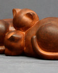 Photo with gray background of brown plaster cast sculpture of two cats sleeping with their heads nestled together from a slight angle