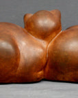 Photo with gray background of brown plaster cast sculpture of two cats sleeping with their heads nestled together