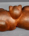 Photo with gray background of brown plaster cast sculpture of two cats sleeping with their heads nestled together