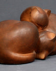 Photo with gray background of brown plaster cast sculpture of two cats sleeping with their heads nestled together