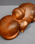 Photo with gray background of brown plaster cast sculpture of two cats sleeping with their heads nestled together