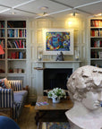 Photo of a colorful living room with blue striped sofas, fireplace, and bookshelves and a plaster cast sculpture of male head of Antinous with crown of leaves in the foreground