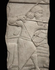 photo of plaster cast relief sculpture of King Ashurbanipal on horseback (only midsection of horse visible) and aiming an arrow in front of him on a black background