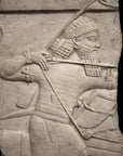photo of plaster cast relief sculpture of King Ashurbanipal on horseback (only midsection of horse visible) and aiming an arrow in front of him on a black background