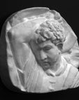 photo of plaster cast sculpture relief of upper body of male with arm raised behind head and holding a hammer with a black background