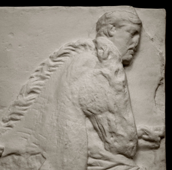 closeup photo of off-white plaster cast relief sculpture of three men on horseback from Parthenon against black background
