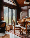 photo of cabin with glass-door wall, table and chairs with hanging lamp above, wood stove, and Victory of Samothrace plaster cast sculpture in the corner on a table