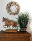 Photo of a plaster cast of a horse with a terra cotta finish on a wicker cabinet with a plant to the right and a metal wreath on the wall above