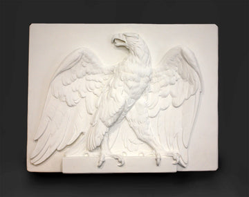 photo of white plaster cast of relief sculpture of an eagle calling, with its head turned toward the right and its wings open on gray background