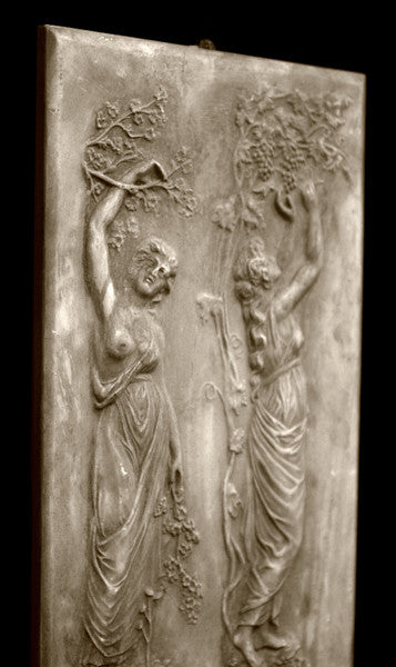 photo with black background of yellowed plaster cast relief sculpture of two robed female figures touching tree branches above their heads