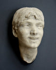 photo of antique plaster cast sculpture of front half of woman's head and neck against black background