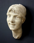 photo of antique plaster cast sculpture of front half of woman's head and neck against black background