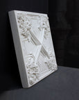 photo of white plaster cast of architectural ornament with geometric lines and leaf patterns against black background