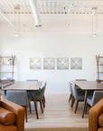 photo of white plaster casts of an architectural ornament in a row on white wall in room with two brown tables and gray chairs, and in the foreground two brown chairs