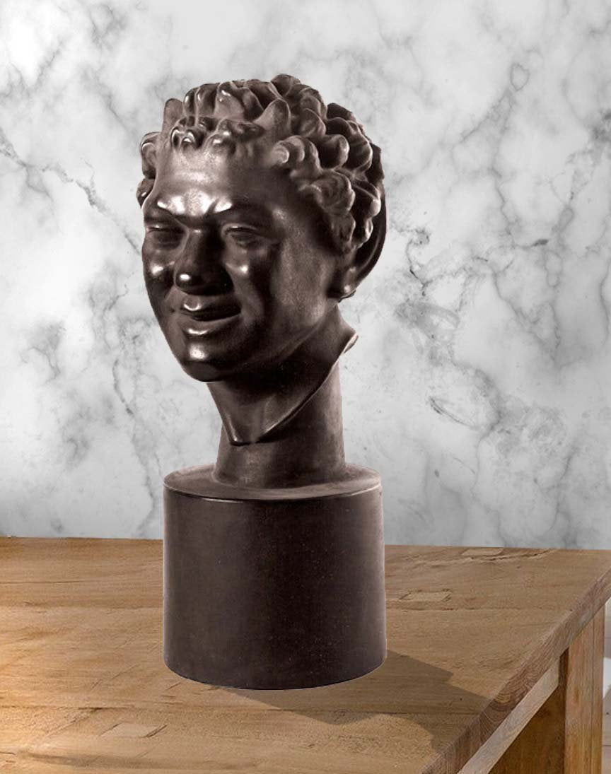 Photo of plaster cast sculpture of faux bronze faun head on wooden table with marble wall behind