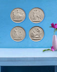 close up of light blue desk with small pink vase with pink flowers against bright blue wall featuring seven off-white plaster cast relief sculptures