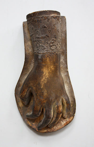 photo of bronze-colored plaster cast sculpture of baby hand with lace sleeve against light gray background