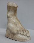 photo of yellowed plaster cast sculpture of right foot on curved surface on gray background