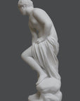 photo of plaster cast of sculpture of partially nude female, namely Venus, leaning forward to wash her left leg with a gray background