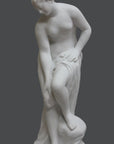 photo of plaster cast of sculpture of partially nude female, namely Venus, leaning forward to wash her left leg with a gray background