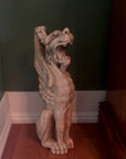 hoto of plaster cast sculpture of imaginary seated winged lion in front of a green wall with white baseboard