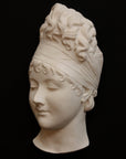 photo with black background of plaster cast sculpture of face of Madame Recamier with high up-do and ribbon over forehead