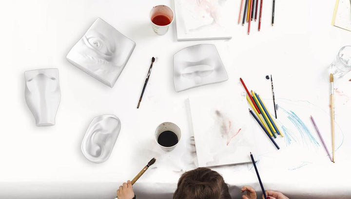 Photo of a top down view of a person's head over a white desk with paints and the eye, ear, nose, and mouth of Michelangelo's David