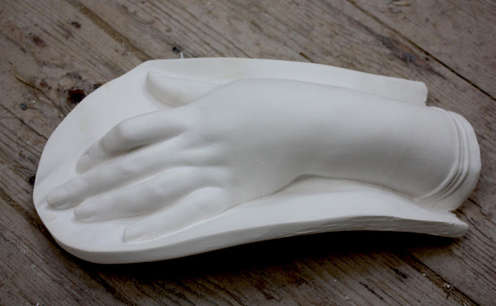 photo of plaster cast of female hand on low curved panel on wood floor
