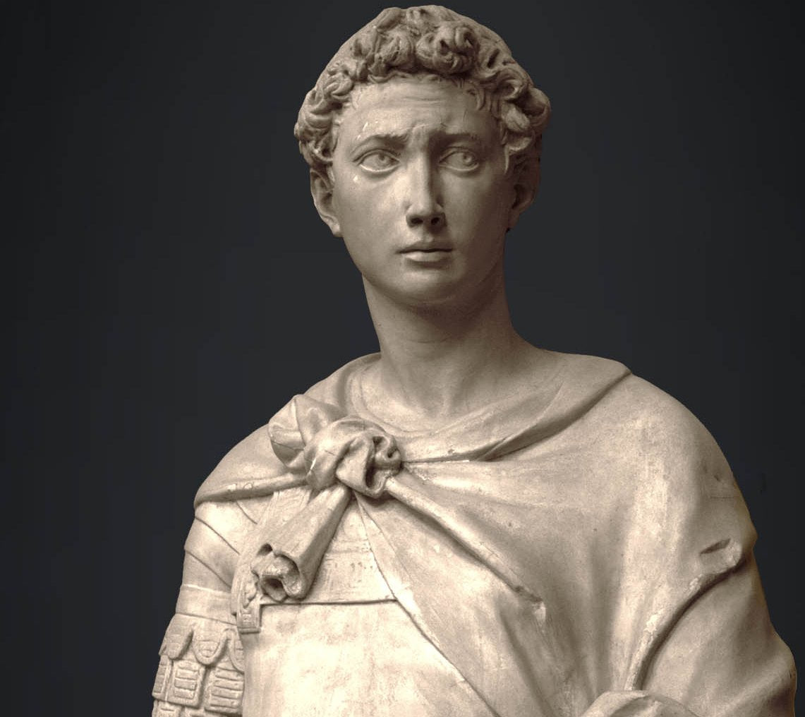 photo of plaster cast sculpture of male figure, namely Saint George, standing in armor and resting shield in front, on dark gray background
