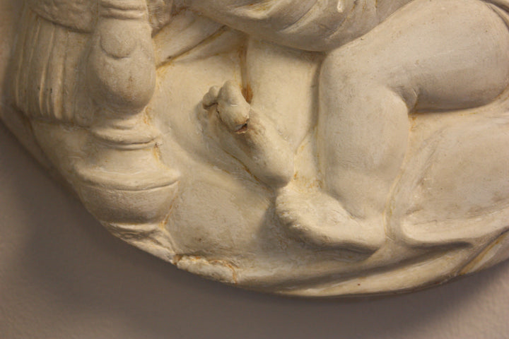 closeup photo of Christ child's feet in plaster cast of relief sculpture featuring the Madonna, Child, and St. John and hanging on a tan wall