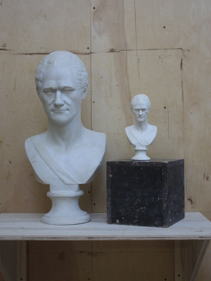 photo of large Alexander Hamilton bust beside a small one atop a black box on a wooden shelf