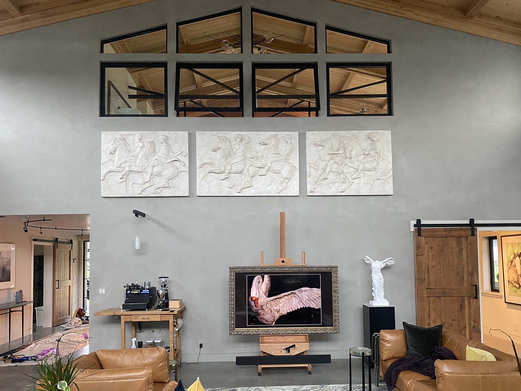 Parthenon-slabs-on-gray-wall-under-large-windows-and-high-ceiling-with-Victory-and-photo-of-swan-and-leather-furniture-and-wood-trim