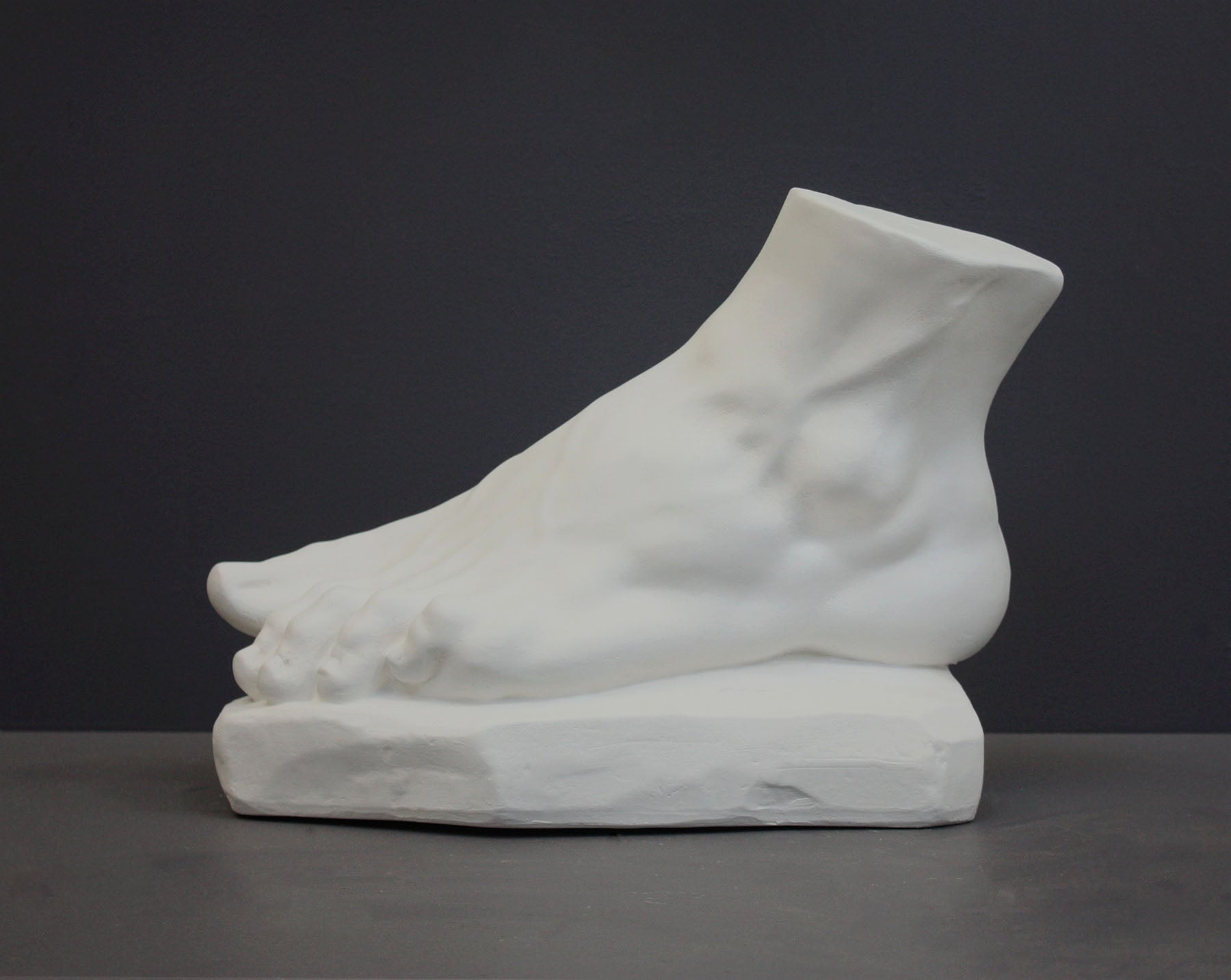 photo of white plaster cast sculpture of left foot on base against gray background