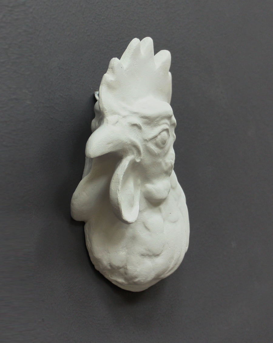 photo of white plaster cast sculpture of a rooster head facing to its right on gray background