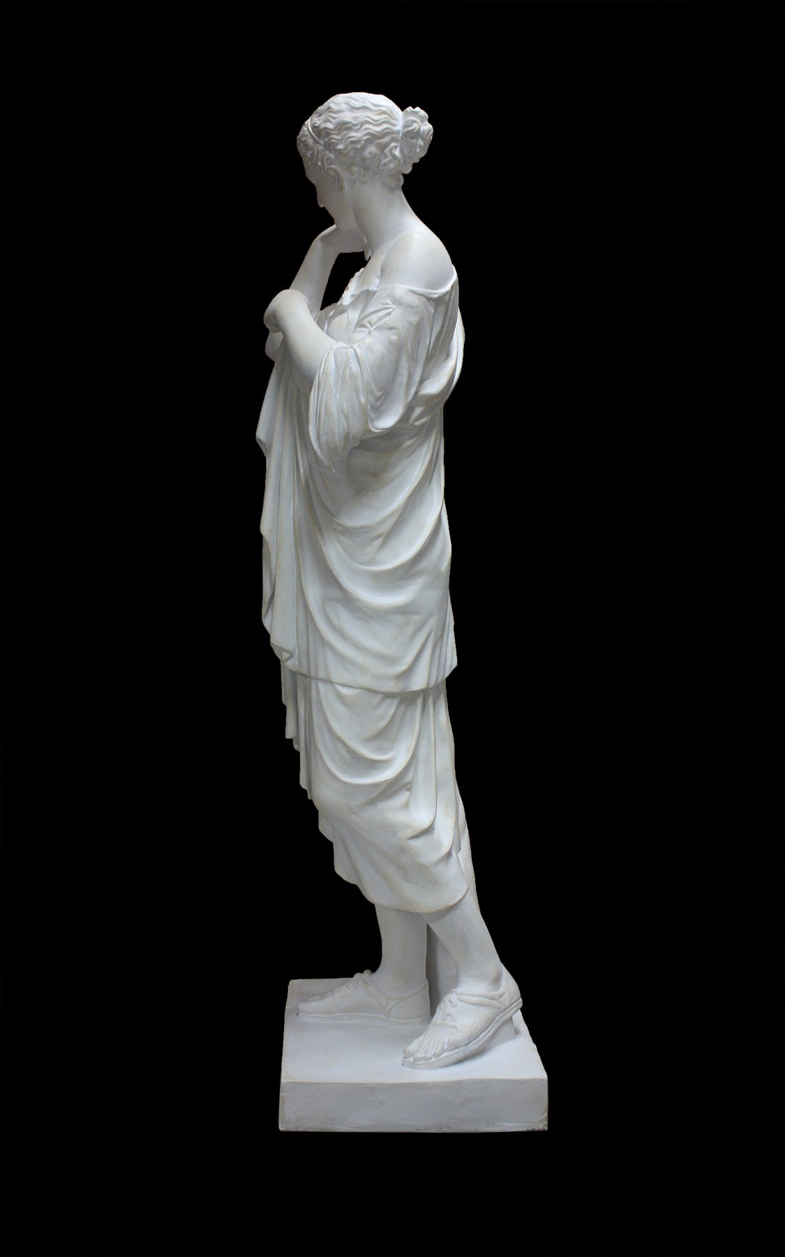 photo of white plaster cast of female figure, namely the goddess Diana, in robes about to clasp two pieces together at proper right shoulder, against black background
