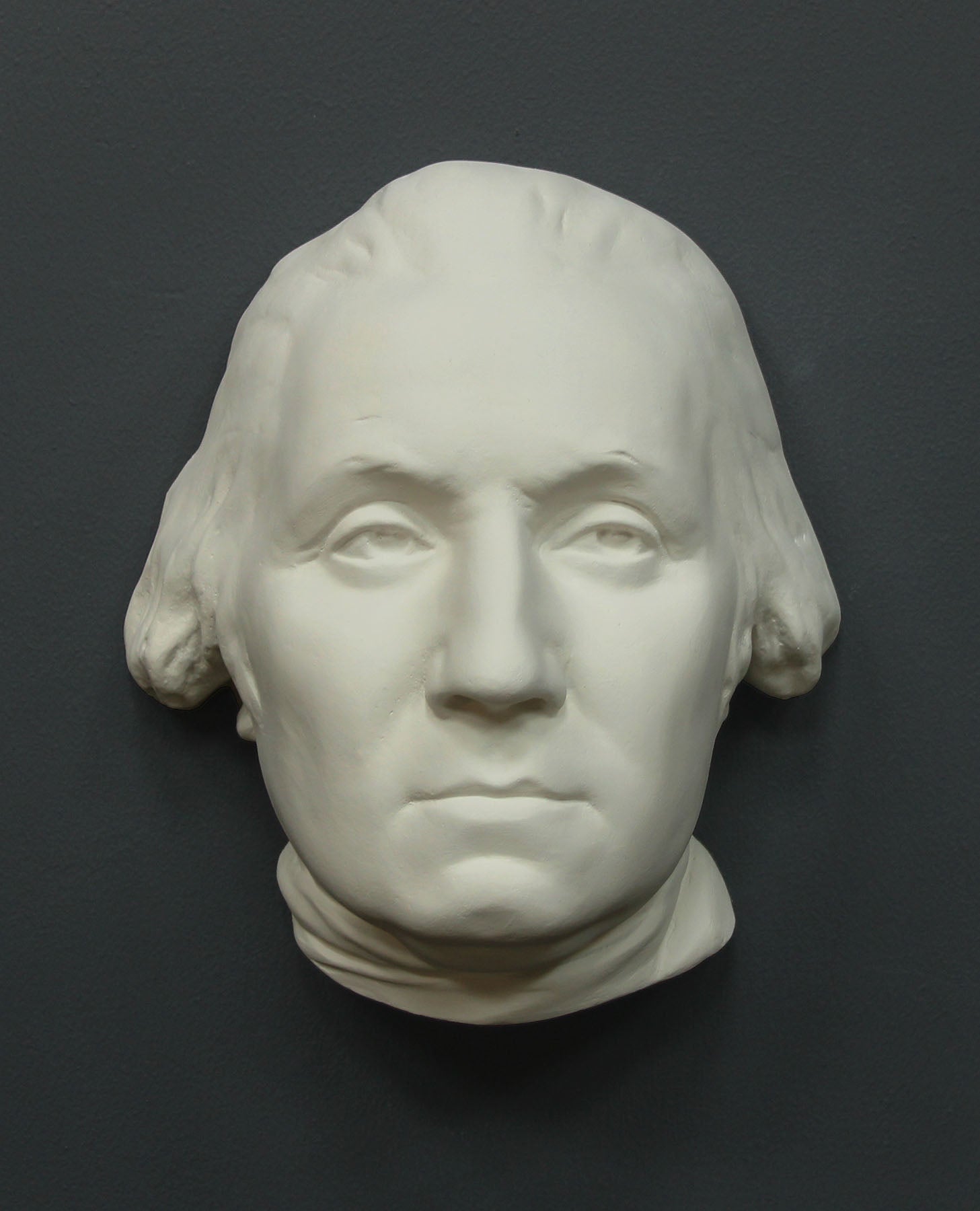 Photo of white plaster cast sculpture of mask/face of male in Revolutionary garb, namely George Washington, on gray background