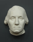 Photo of white plaster cast sculpture of mask/face of male in Revolutionary garb, namely George Washington, on gray background