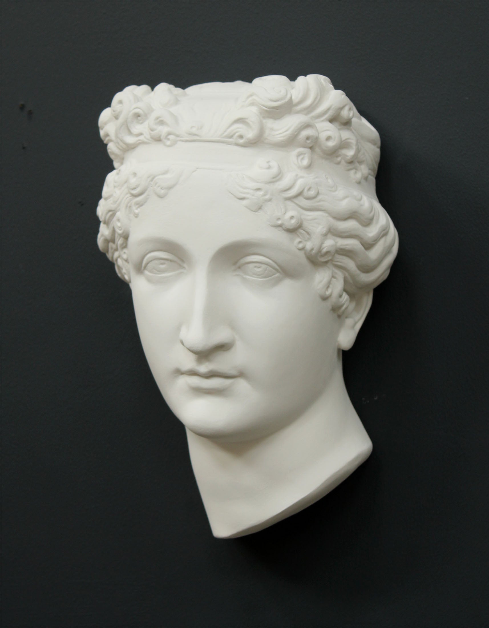 Photo of white plaster cast sculpture of mask/face of female with headband, namely Pauline Bonaparte, on gray background